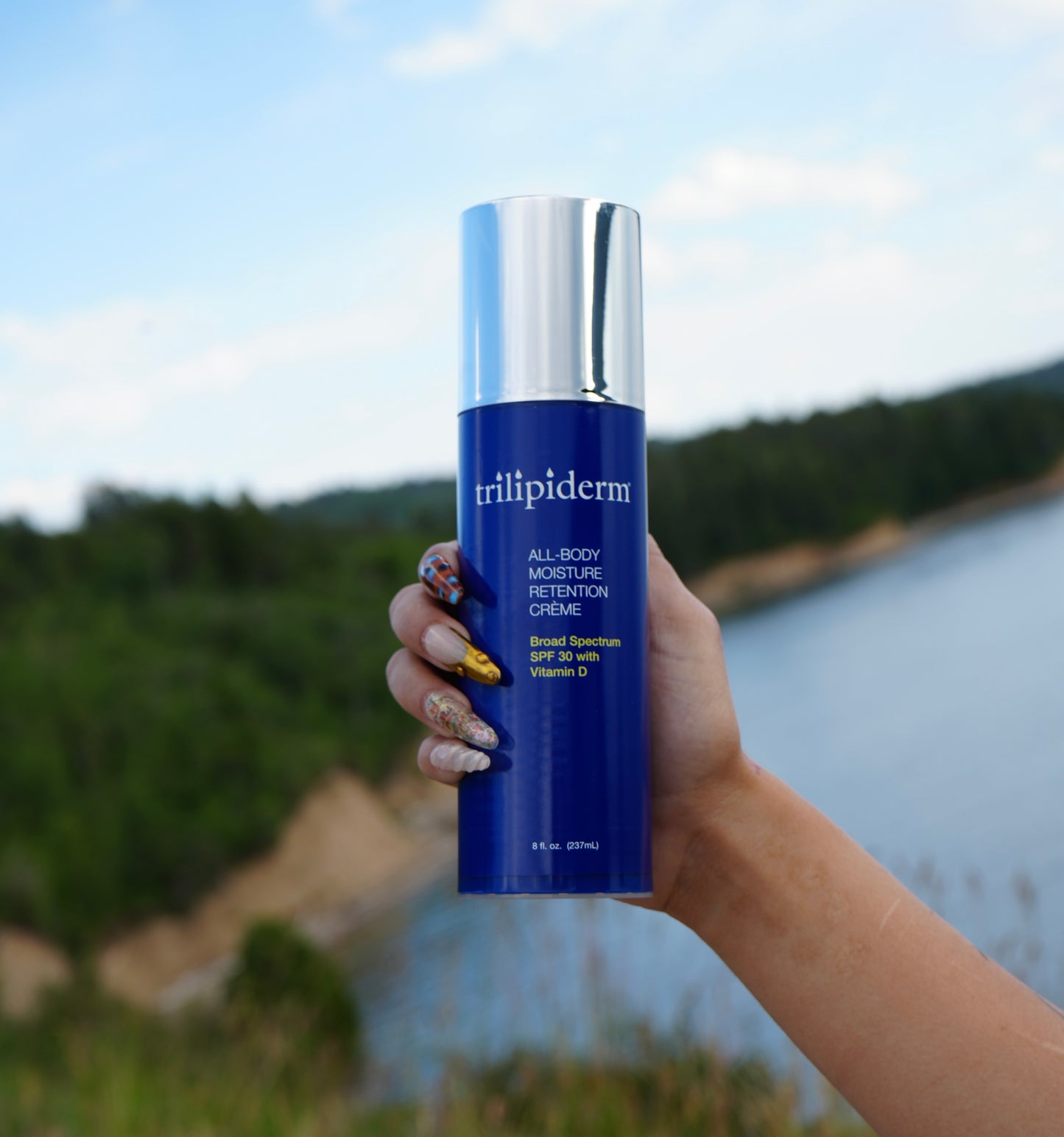 Hand holding a blue bottle of trillipiderm product with a scenic background