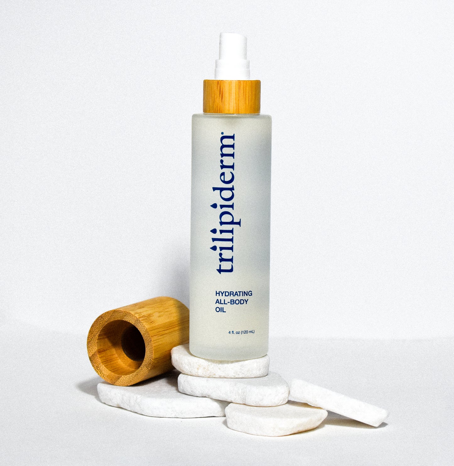 hydrating all body oil in clear glass bottle displayed on white rock with bamboo cap on side on white background