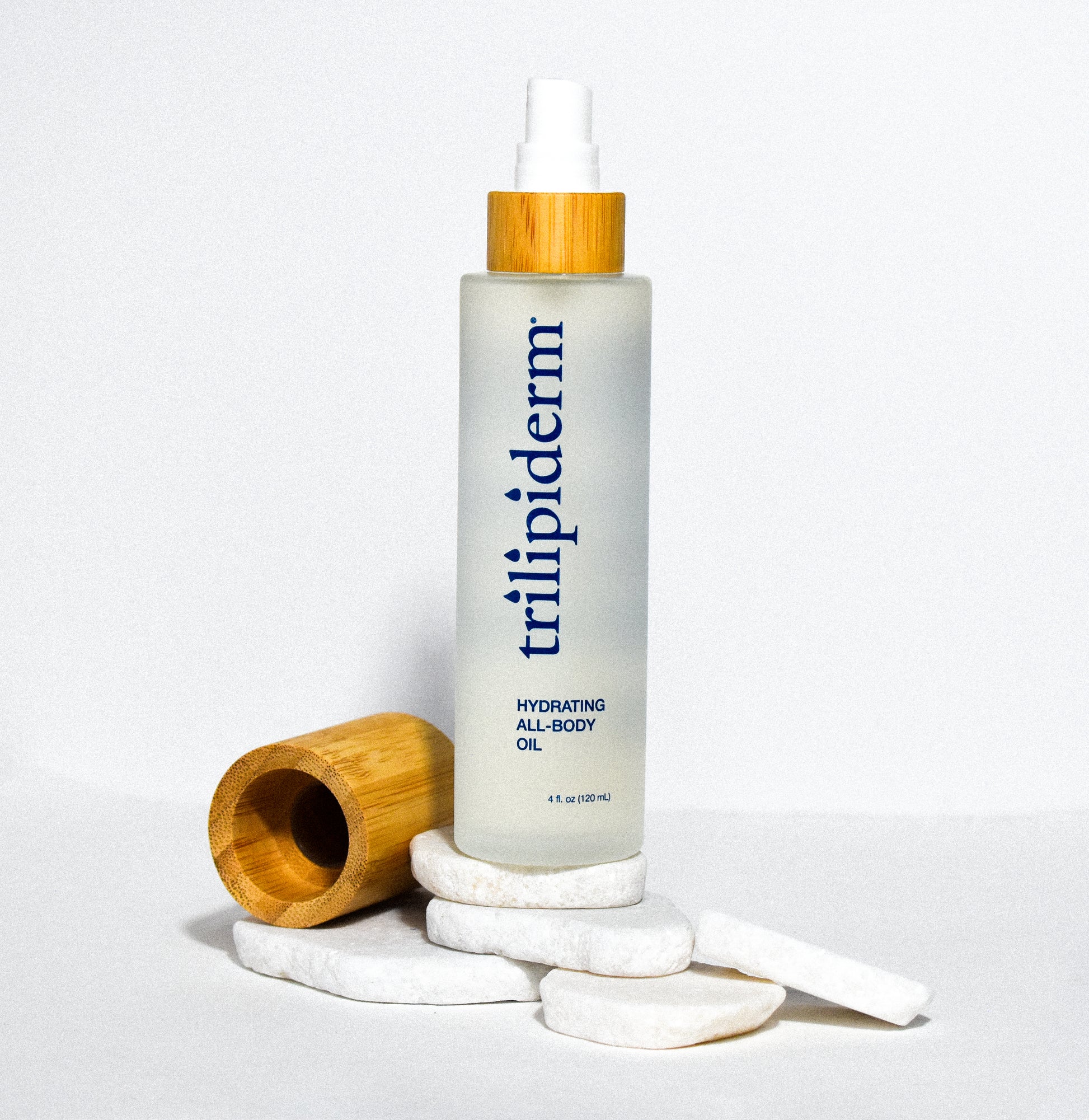 hydrating all body oil in clear glass bottle displayed on white rock with bamboo cap on side on white background