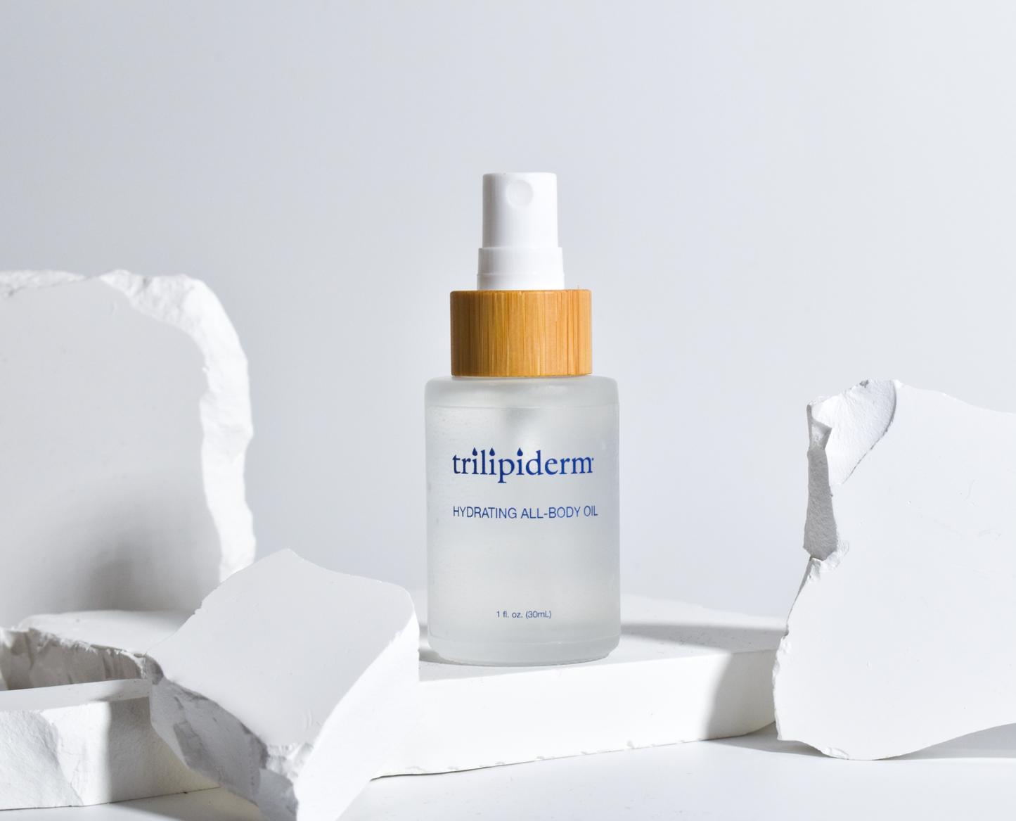 hydrating all body oil in clear glass bottle displayed on white rock with spray bottle applicator brimmed with bamboo white background