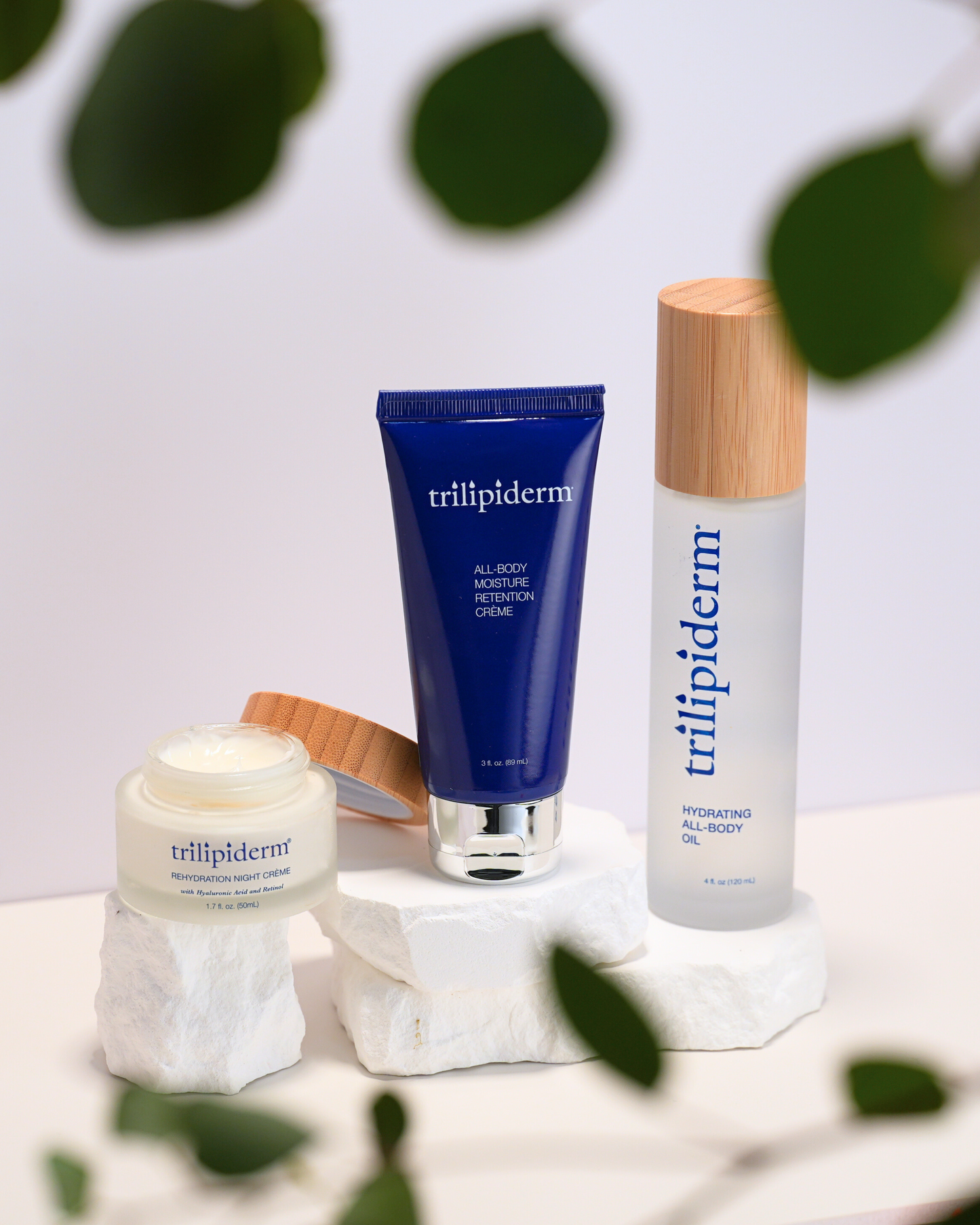 Trillipiderm skincare products on a white surface with green leaves in the background