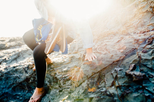 Two people scrambling over sun-drenched coastal rocks at Grand Teton, golden light flaring behind them