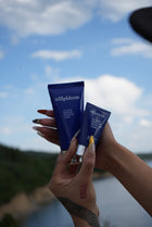 Two blue skincare products held against a blurred natural background