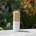 Skincare bottle with wooden cap on a stone surface with a blurred green plant background