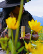 Person holding a bottle of serum surrounded by yellow flowers outdoors