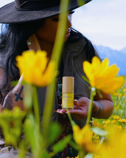 Person holding a bottle of serum surrounded by yellow flowers outdoors