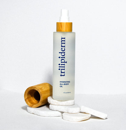 hydrating all body oil in clear glass bottle displayed on white rock with bamboo cap on side on white background
