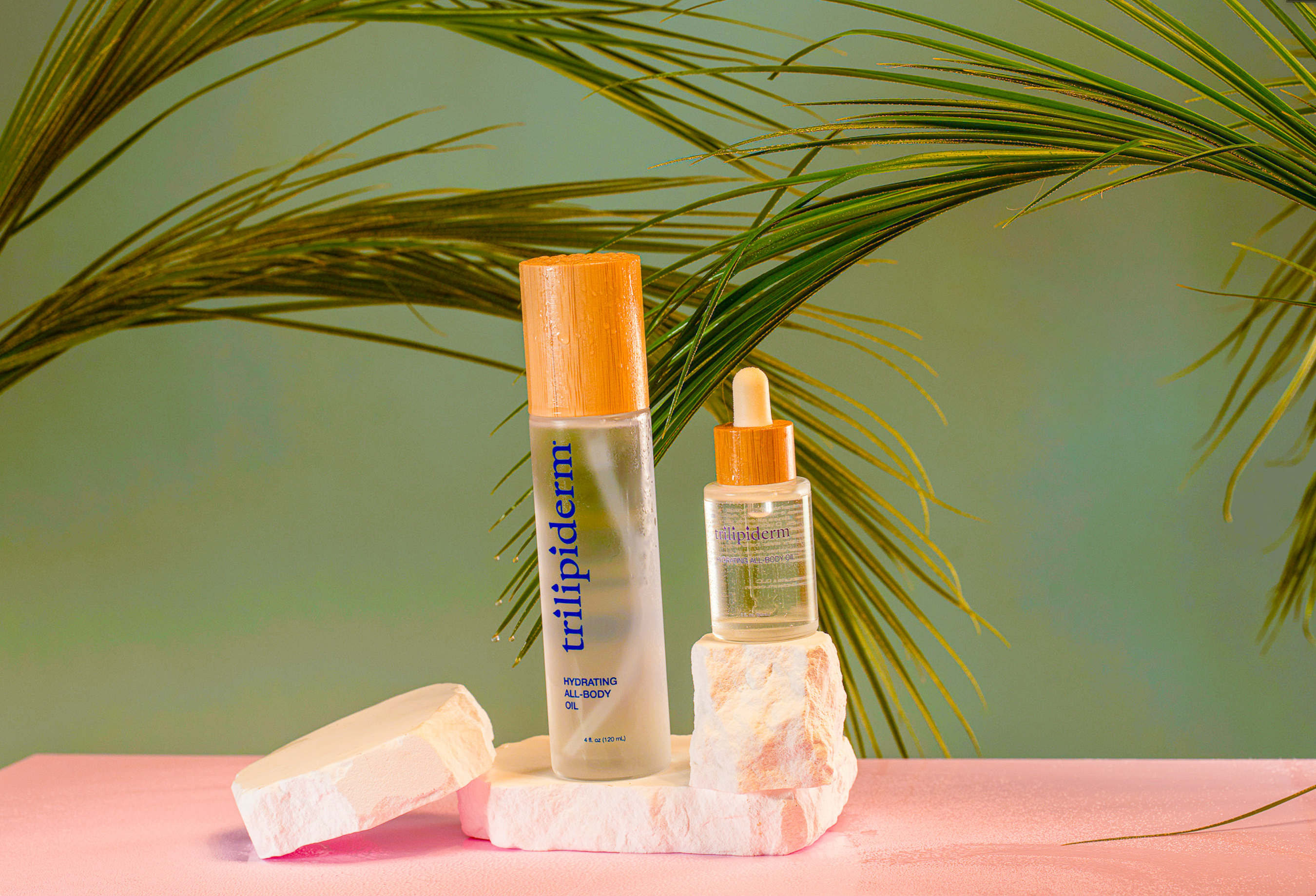 Hydrating all-body oil on white rock with hydration features and palm leaves in backround, pink & green theme