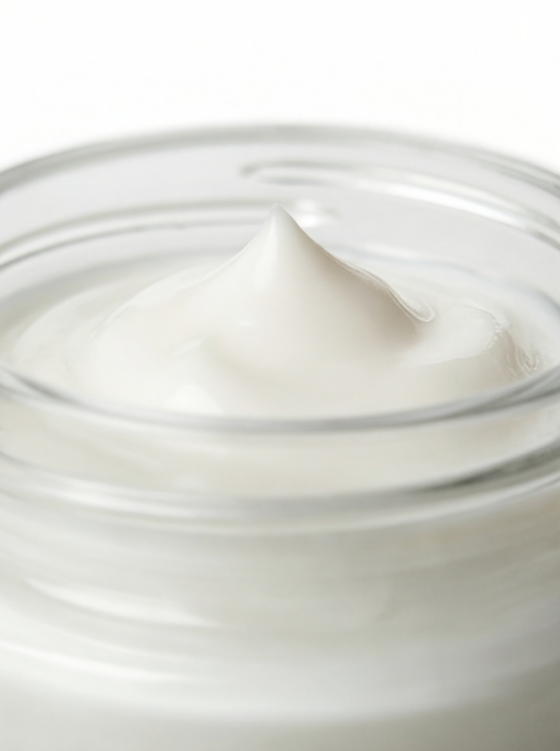 Close-up of Trilipiderm Rehydration Night Crème texture in a clear glass jar, showing a smooth, velvety peak of cream with a soft glossy finish—rich overnight moisturizer with hyaluronic acid and retinol.