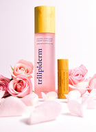 trilipiderm pink toner with clear glass bottle and bamboo cap and bamboo encased lip balm surrounded by pink flowers with a pink hued background