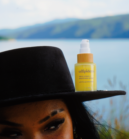 Person wearing a black hat with a bottle of 'trillipiderm' serum on top, set against a scenic background.