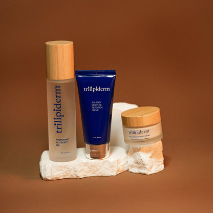 Trilipiderm Barrier Rescue Trio featuring Hydrating All-Body Oil, All-Body Moisture Retention Crème, and Rehydration Night Crème for barrier support, deep hydration, and moisture retention. Brown studio backdrop.