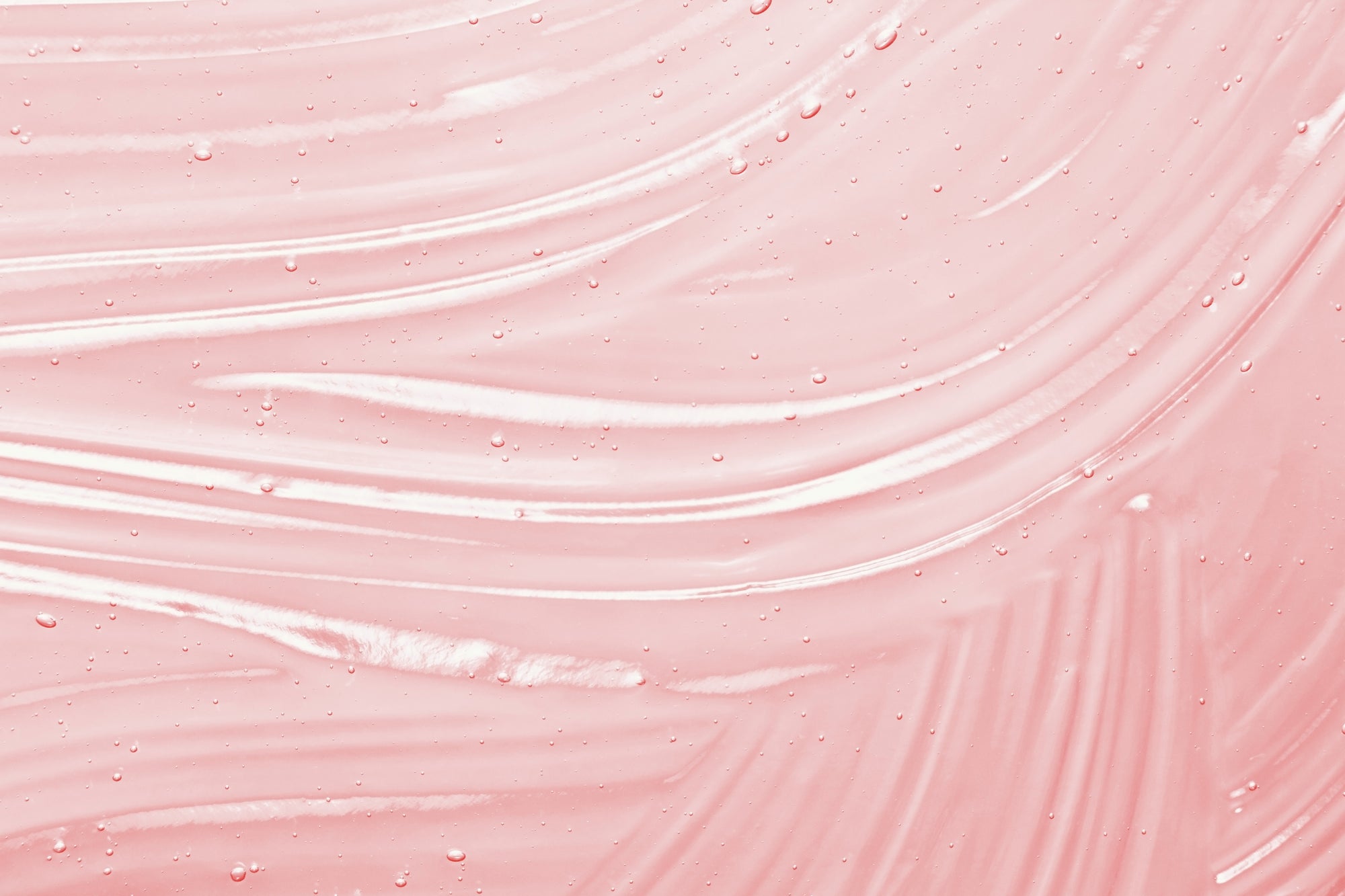 Close-up of pink niacinamide serum textured surface with wavy swatch patterns of hydrating skincare serum