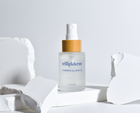 hydrating all body oil in clear glass bottle displayed on white rock with spray bottle applicator brimmed with bamboo white background