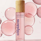 Trilipiderm Youthful Complexion Rosehip Toning Elixir spray toner in a frosted pink bottle with bamboo cap, standing on a glossy surface with translucent pink bubble spheres in the background. Hydrating, antioxidant-rich facial mist toner designed to refresh dull, dehydrated skin, support a healthy-looking glow, and soften the look of texture. Use after cleansing, before serums, or throughout the day over makeup for a dewy, revived finish. Luxury clean skincare aesthetic, minimalist studio lighting, closeup