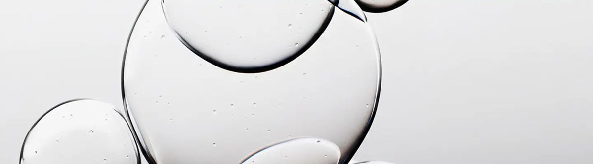 A close-up studio shot of several transparent glass or acrylic droplets and bubbles on a light gray background.