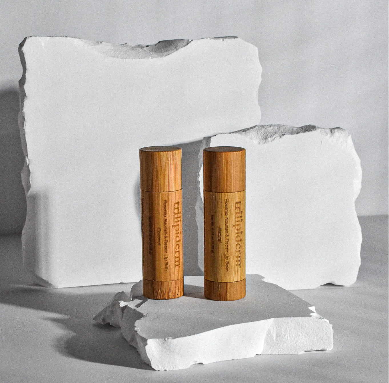 Trilipiderm Bamboo Lip Balm in Rosehip and Coconut displayed on white sculpted stone — sustainable natural lip care with a minimalist aesthetic
