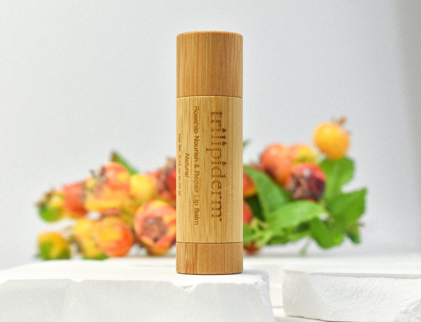 Trilipiderm Rosehip Nourish & Repair Lip Balm in bamboo packaging displayed with rosehip fruit background — natural lip care with botanical ingredients.