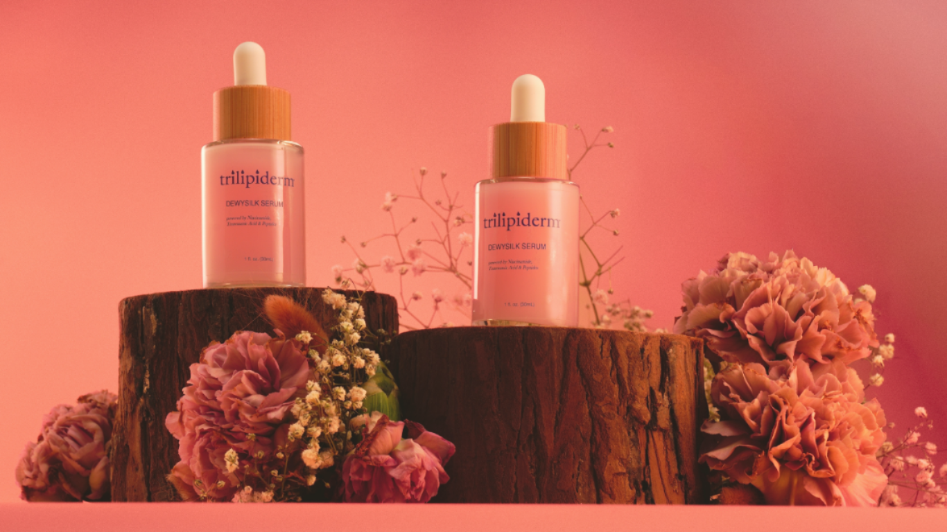 Trilipiderm DewySilk Serum with niacinamide and botanicals displayed with pink flowers on wood blocks