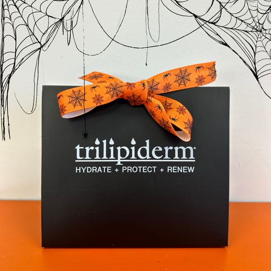 Trilipiderm black gift bag with orange spiderweb ribbon and Halloween web decorations, featuring the Hydrate + Protect + Renew logo.