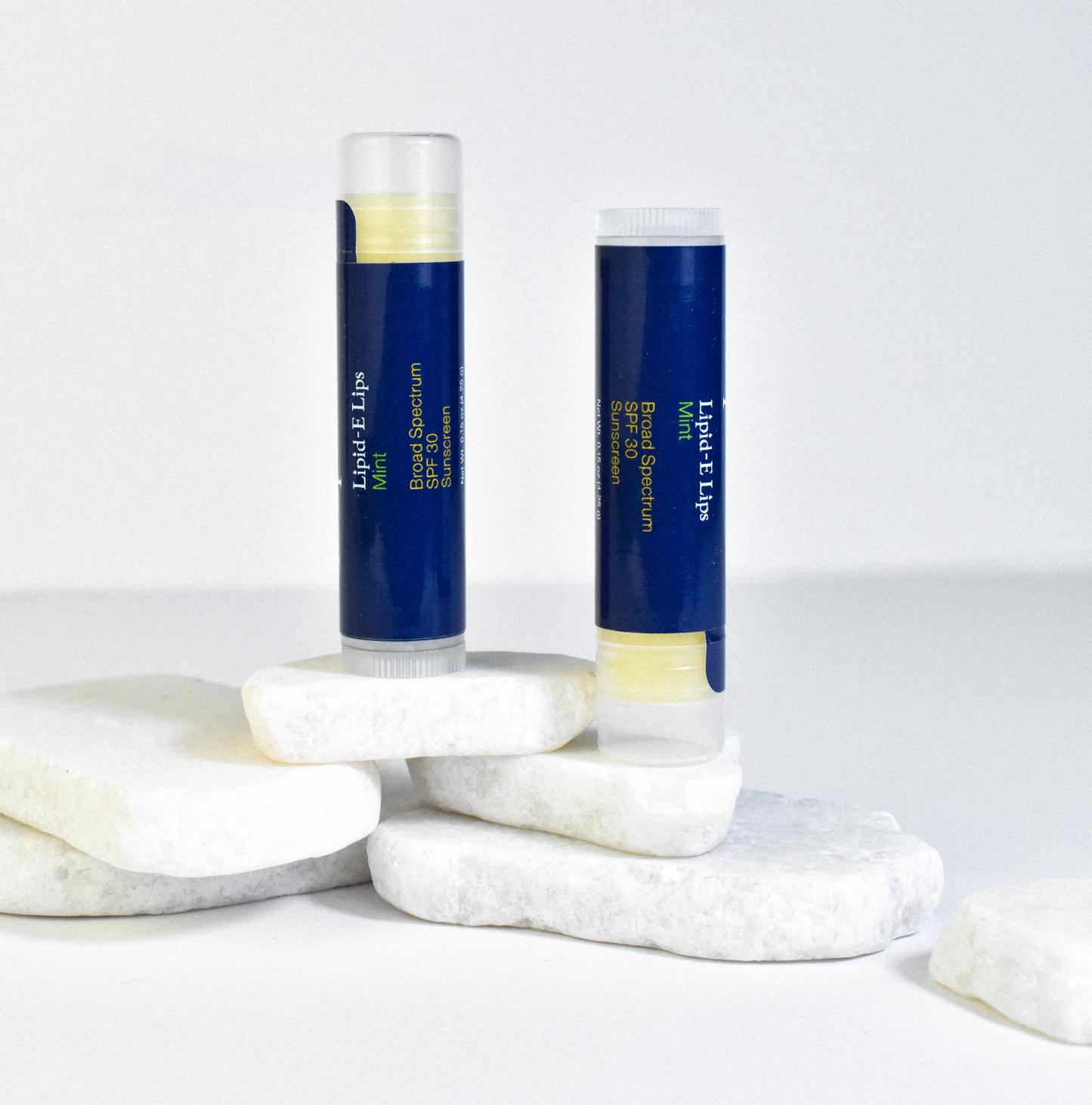 Trilipiderm Lipid-E Lip Balm Mint SPF 30 displayed on white stone slabs — hydrating lip care with broad spectrum protection