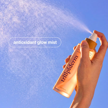 Hand holding a bottle of 'tripliderm' antioxidant glow mist against a blue sky background.Trilipiderm Youthful Complexion Rosehip Toning Elixir product overview highlighting barrier-boosting glass glow mist with instant hydration, smoother texture refinement, and skin barrier support. Frosted blush bottle with bamboo cap surrounded by pink liquid splash on white background. Luxury antioxidant facial toner for radiant skin.