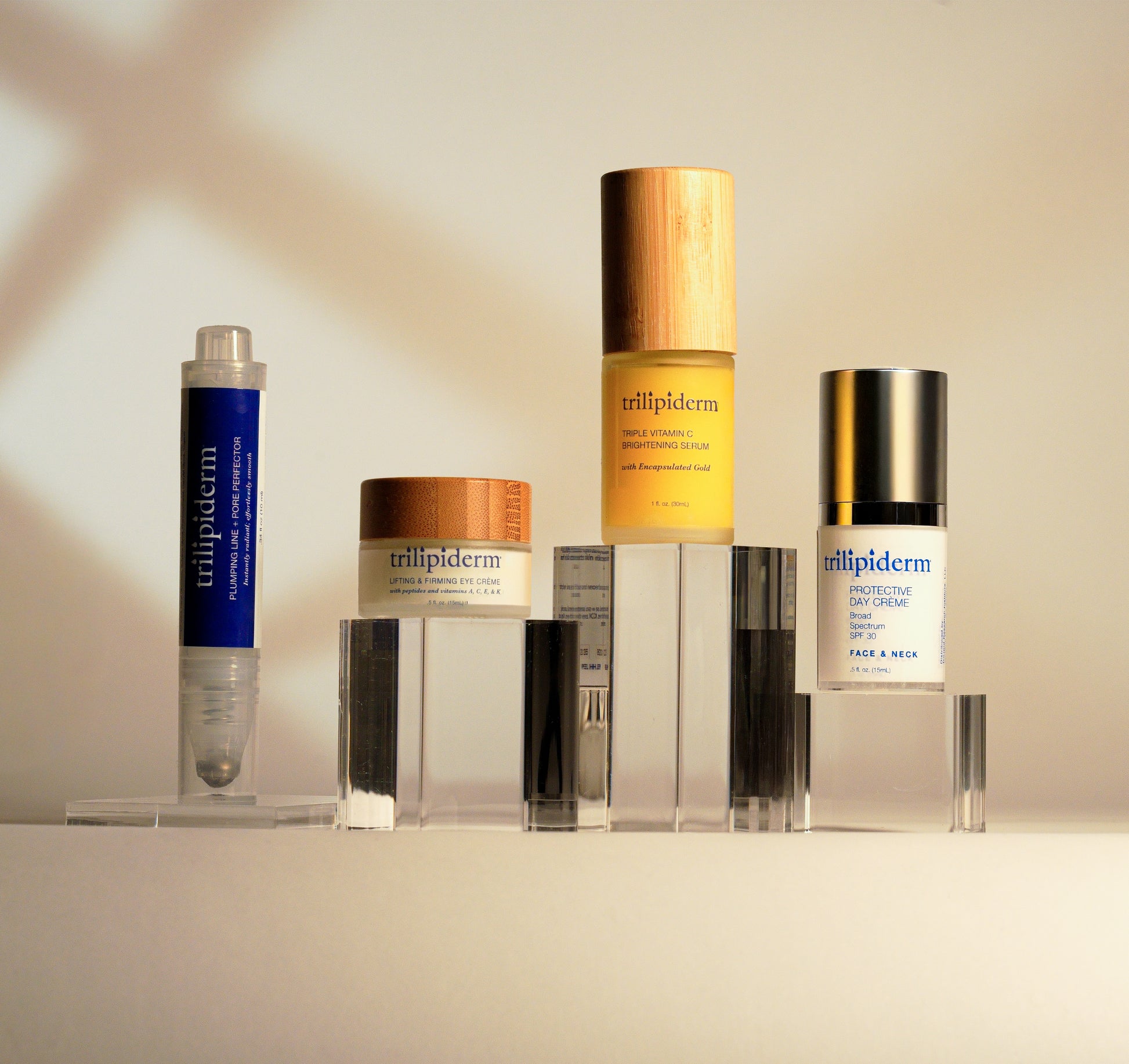 Trilipiderm eye crème, plumping perfector, vitamin C serum, and day crème shown with product textures on a clean white background.