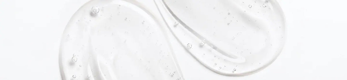 A close-up of a clear, glossy gel or serum swatch with small bubbles on a white background.